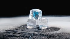 Three ice cubes melting on a black surface with water droplets.